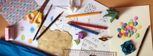 Bunstifte, Origamis, Papiere, Schere, Lineal, Ausmalbild, Schatzkarte bunt durcheinander gewürfelt.